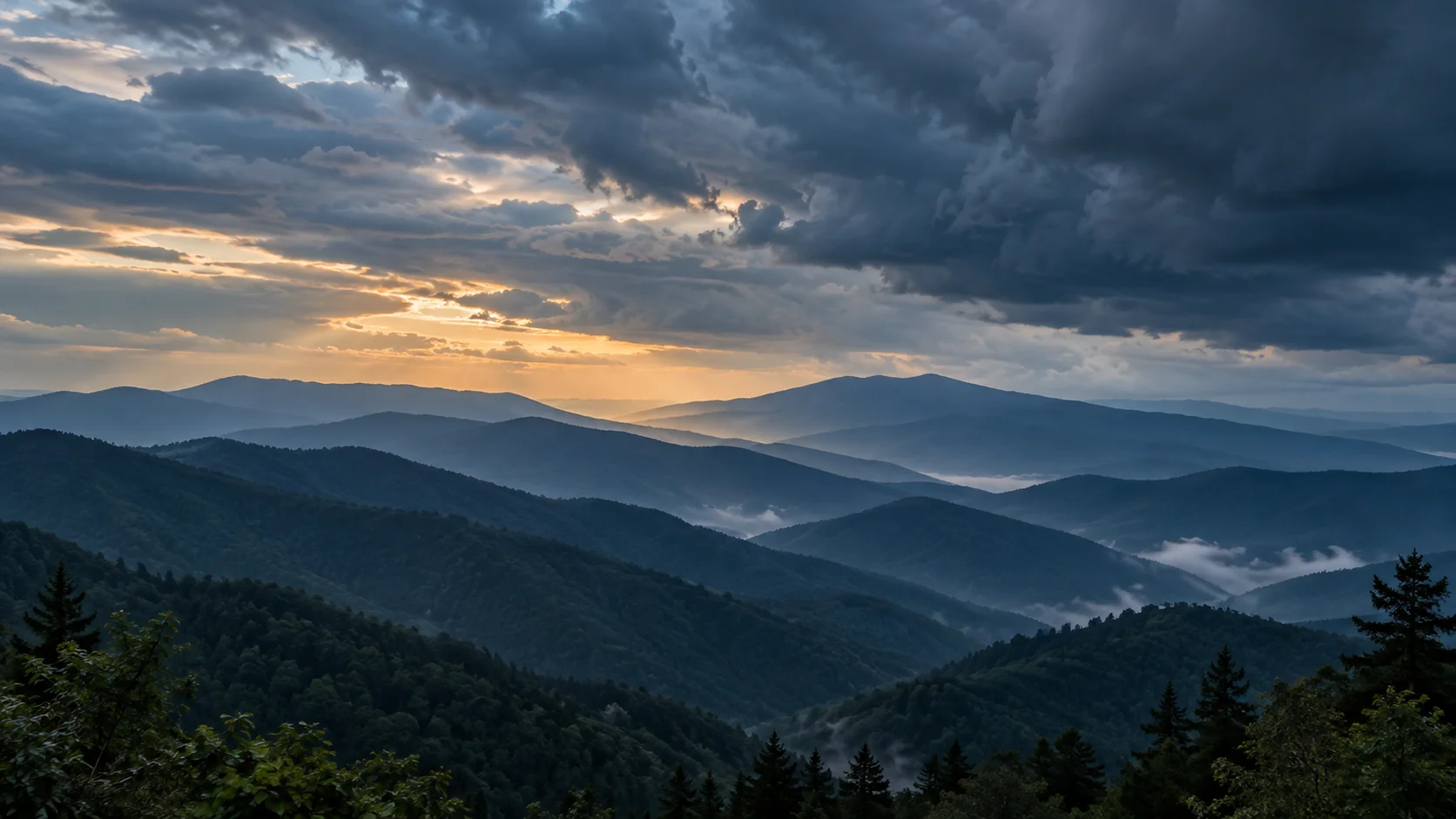 Layered mountain ridges beneath approaching clouds and a break of evening light